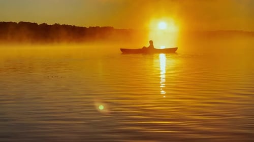 Kayaker Floats on Calm Water Through the Morning Fog Above the Water at Sunrise the Silhouette of a