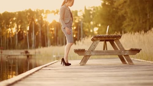 Sexy Business Woman in Suit Bends Over and Uses Laptop Outdoors During Sunset on Lake