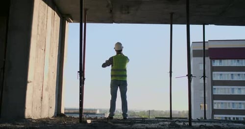Engineer Builder on the Roof of the Building at Sunset Stands in VR Glasses and Moves His Hands