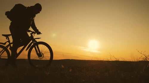 Die Silhouette des Mountainbike-Fahrers auf dem Hügel mit Fahrrad bei Sonnenuntergang. Sport, Reisen und
