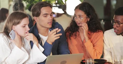 Young Creative Coworkers Talking and Looking at Laptop Screen While Sitting in Cafe. Concentrated