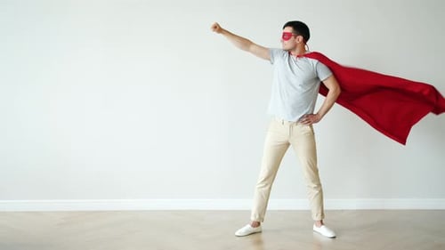 Porträt eines Superhelden in flatterndem roten Umhang und Maske stehend mit erhobenem Arm