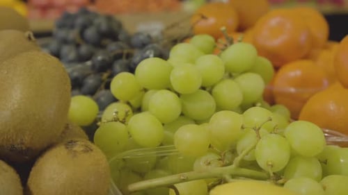 Close-up of Fresh Delicious Green Grapes, Kiwi Fruits and Tangerines in Grocery Store. Tasty