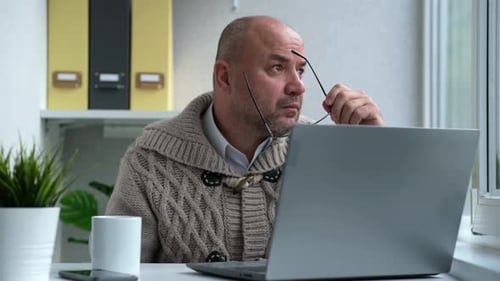 Geschäftsmann mittleren Alters mit Brillen, der mit dem Computer arbeitet und aus der Ferne zu Hause oder im Büro sitzt