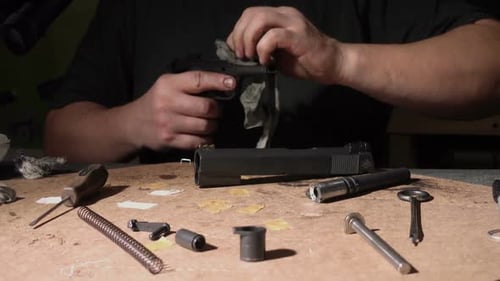 Man Cleaning Disassembled Pistol on Workbench