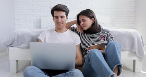 Couple Using Laptop and Tablet in Bedroom