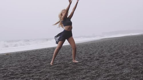 Flexible and Beautiful Woman Dancing By the Black Beach on a Windy Day