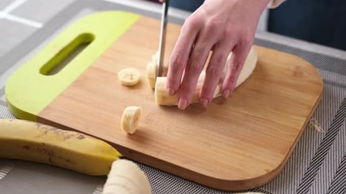Woman Slices Banana on Wooden Cutting Board
