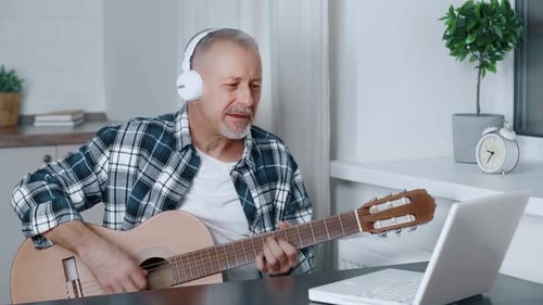 Man Plays Guitar at Home with Laptop