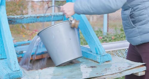 Person Lifts Bucket of Drinking Water From Well By Turning Handle of Old Mechanism
