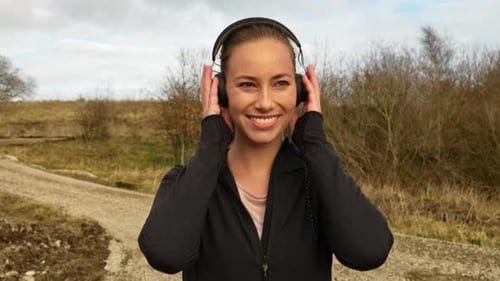 Woman Puts on Headphones in Nature Setting