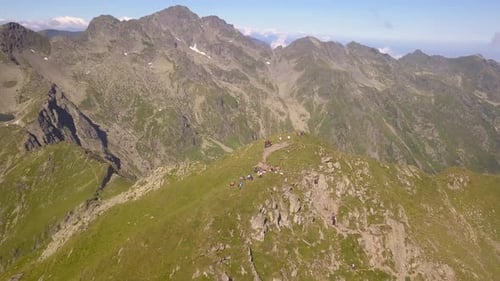 Drone orbiting high over remote mountain peak with hikers and backpackers on summit. Clear sky above