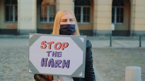 Une femme blonde portant un masque de protection proteste pour mettre fin aux préjudices en tenant un bateau à vapeur