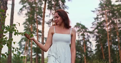 Beautiful Girl Touches Tree Branches and Walks Through the Forest