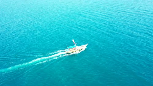Barco turístico que navega lentamente a través de la superficie del mar azul con agua vibrante que refleja el cielo azul brillante