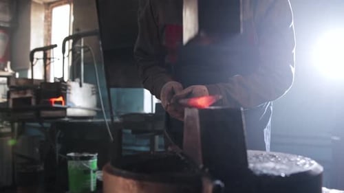 Man Blacksmith verdünnt ein heißes längliches Stück Metall unter einer automatischen Pressmaschine