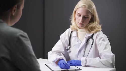 Blonde Doctor Consults Patient Writing on Clipboard