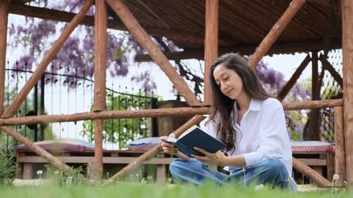 Young Woman Reading Book Outdoors in Garden
