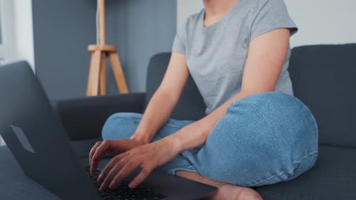 Woman Types on Laptop at Home on Sofa