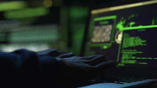 Hacker trabalhando na criação de software malicioso, digitando ativamente no teclado do laptop