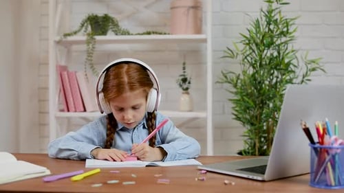 Girl Does Homework at Desk Wearing Headphones