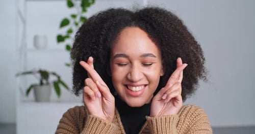 Sincere African American Girl with Afro Curls Hairstyle Smiling Crossing Fingers Making Gesture of