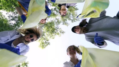 Grupo de amigos activistas arrojan mucha basura en una bolsa. Toma de fotos de abajo hacia arriba