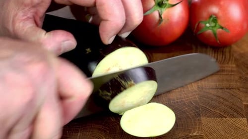 Slicing Eggplant Into Circle on Wooden Cutting Board with Knife on Domestic Kitchen