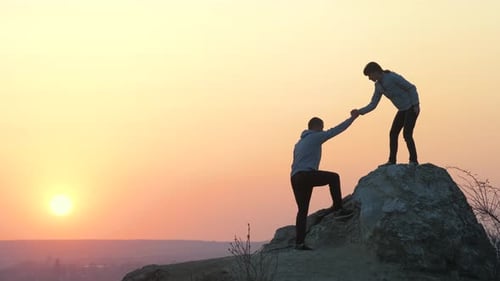 Man Helps Woman Climb Hill at Sunrise