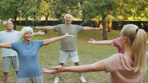 Seniors Stretching with Instructor in Green Urban Park