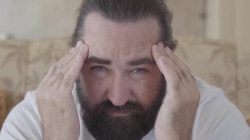 Close Up Portrait of a Bearded Man Who Is Suffering From a Headache, Rubbing His Head with His Hands