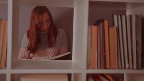 A Student is Reading a Book in the Library Behind the Bookshelves