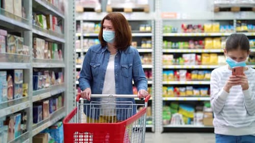 Mãe e filha com máscaras andando entre os corredores do supermercado