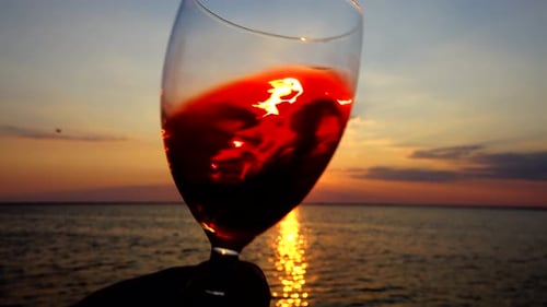 Wine in a glass against the background of the sunset over the sea