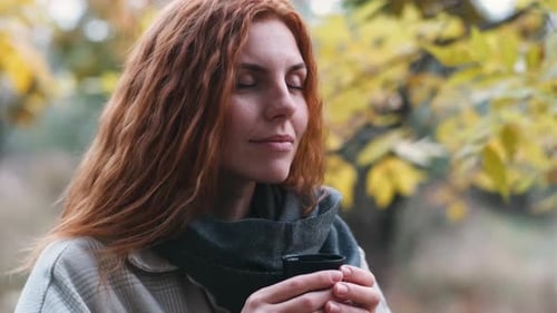 Beautiful Redhaired Woman Drinks Tea From Thermos in the Autumnal Forest