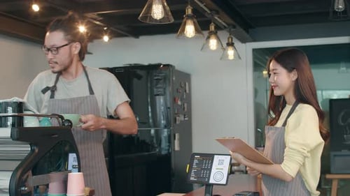 Asia female and male barista waiter taking order from customer standing together behind bar counter.