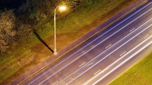 Nachtverkehr von vorbeifahrenden Autos auf der Straße im Licht von Laternen, Zeitraffer