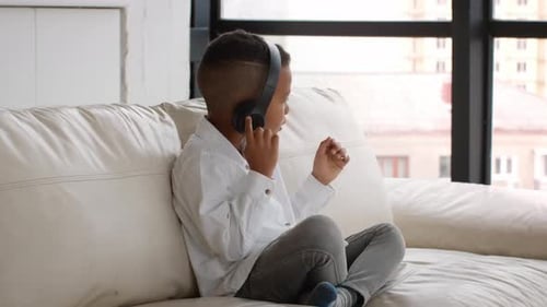 Boy Listens to Music on Headphones on Couch