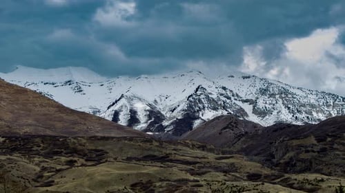 Time Lapse of a dramatic cloudscape above snow-covered mountains with foothills in the foreground in