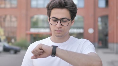 Man Looks at Wristwatch then Shrugs in Urban Setting