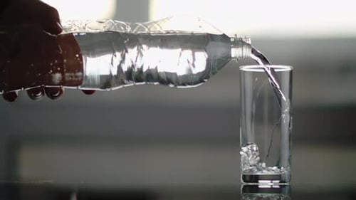 Männliche Hand mit einer Plastikflasche gießt sauberes Wasser in einen Glasbecher