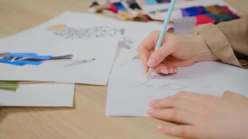 Close up of female designer using pencil and sheet of paper for fashion sketches