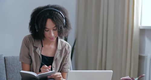 Young Freelancer Girl Sits at Home in Room in Office, Wears Head Microphone and Headphones, Listens