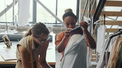 Schneiderinnen legen im Schneiderstudio Stoff auf Schaufensterpuppe
