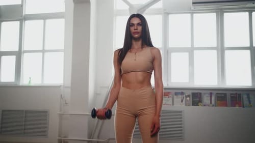 Attractive Slim Woman in Sportswear Lifts Dumbbells for Biceps in the Gym