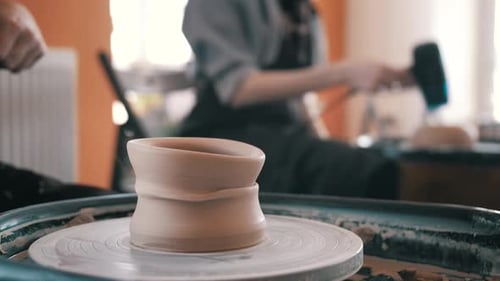 Master is cutting clay cup from potter's wheel, close-up in workshop. She is using wire, and moving