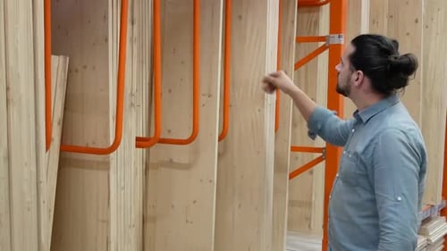 Young Man Selecting Wood Boards in a Hardware Store or Warehouse