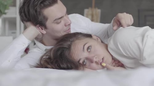 Young Couple Lying in Bed Close-up. Girl Offended and Turned Away From the Man. Difficulties in the