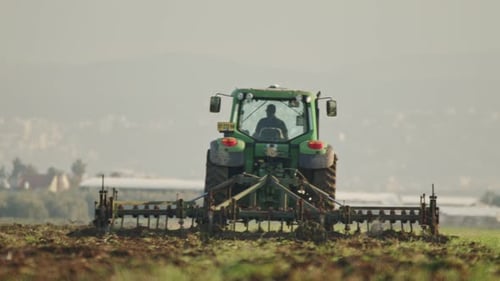 Tractor cultivating a green field in slow motion.