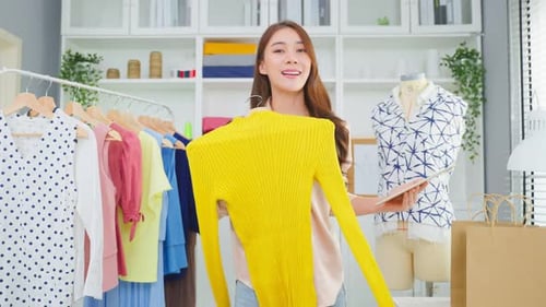 Asian beautiful woman sell cloth product online live streaming at home.